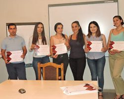 young adults holding TEFL certificates stand with their instructor in front of a decorative stone wall carving—a cozy scene celebrating the completion of a 120‑hour TEFL training.
